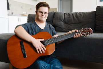 Young man with down syndrome playing guitar while sitting on floor