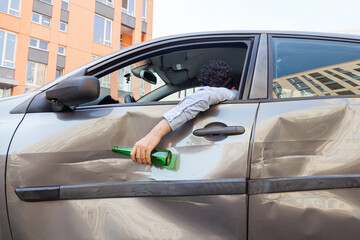 Drunk unknown person behind wheel sleeping in dented car after road accident and holding bottle with alcohol beverage in hand, sleeping in automobile, traffic violation due drunk driving. Outdoor shot - obrazy, fototapety, plakaty