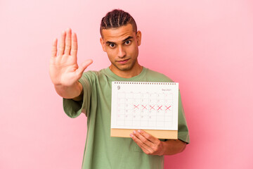 Young venezuelan man holding a calendar isolated on pink background standing with outstretched hand...