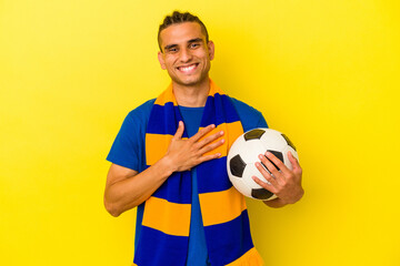 Young venezuelan man watching soccer isolated on yellow background laughs out loudly keeping hand on chest.