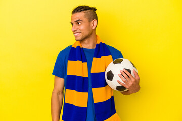 Young venezuelan man watching soccer isolated on yellow background looks aside smiling, cheerful and pleasant.