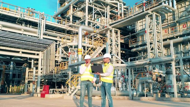 Oil industry, petrochemical factory, refinery concept. Engineers are talking next to the pipes of the oil refinery plant