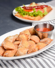 Fried dumplings stuffed with meat and served with tomato sauce on a white plate.