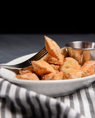 Fried dumplings stuffed with meat and served with tomato sauce on a white plate.