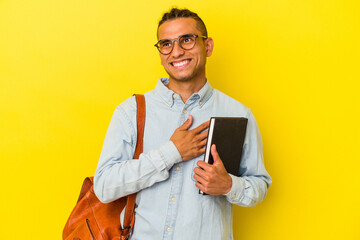 Young venezuelan student man isolated on yellow background laughs out loudly keeping hand on chest.