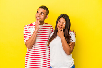 Naklejka premium Young latin couple isolated on yellow background looking sideways with doubtful and skeptical expression.