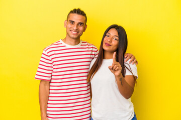 Young latin couple isolated on yellow background showing number one with finger.