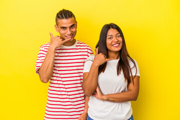 Naklejka premium Young latin couple isolated on yellow background showing a mobile phone call gesture with fingers.