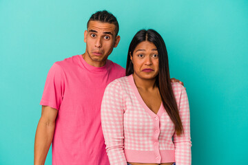 Fototapeta premium Young latin couple isolated on blue background shrugs shoulders and open eyes confused.