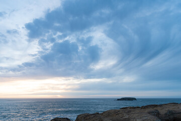Fototapeta na wymiar ocean water with stony shore and cloudy sunset sky, nature