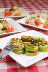 Apetizer from tomatoes, zucchini and mozzarella cheese served on a white plate with other dished on the table.