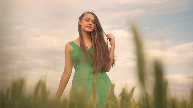 A teenager girl happily walks through the green field of grain crops. The girl's hair develops in the wind. Happy family free dream people outdoors concept of childhood. The man is looking forward.