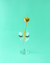 A glass cup with eyelashes and a gold tube with a heart. Celebration. Turquoise background.