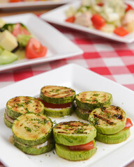 Appetizer from tomatoes, zucchini and mozzarella cheese served on a white plate with other dished on the table.
