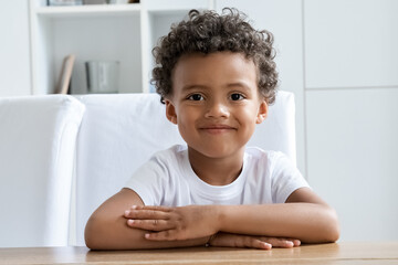 Cute happy smiling preschool boy child student sitting at desk looking at camera