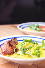 Risotto with meat steak and sauce served in a white plate on a rustic wooden table.