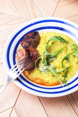Risotto with meat steak and sauce served in a white plate on a rustic wooden table.