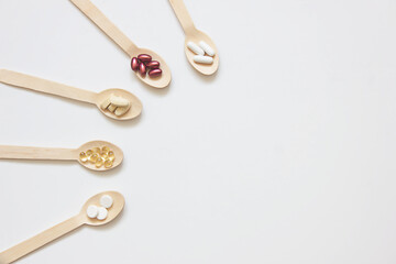 Dietary supplements and vitamins on wooden spoons on a white background. Copy space. The concept of a healthy lifestyle. Place for text.