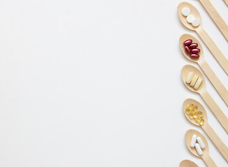 The concept of taking care of your health and healthy lifestyle. Banner. Supplements and vitamins on wooden spoons on a white background.