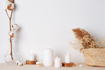 Home decoration with candles, basket and flowers over white wall. Interior design concept. Close up, copy space