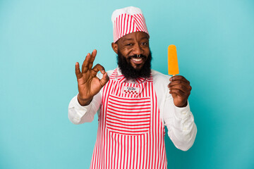 African american ice cream maker man holding an ice cream isolated on blue background cheerful and confident showing ok gesture. - obrazy, fototapety, plakaty