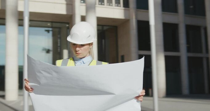 Architect in protective helmet holding blueprint in front of office building