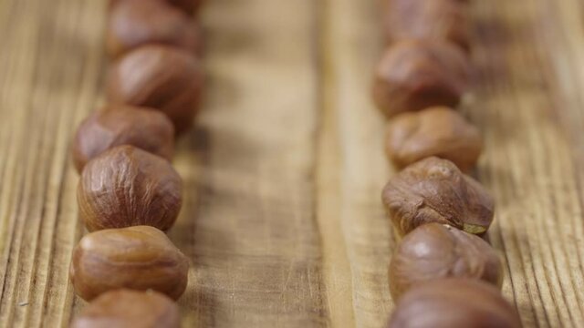 Sliding shot of dried hazelnuts lying in row on textured wooden table surface. Close up whole brown hazel kernels form two lines on table. Organic healthy food background. Slow motion ready 59.94fps.