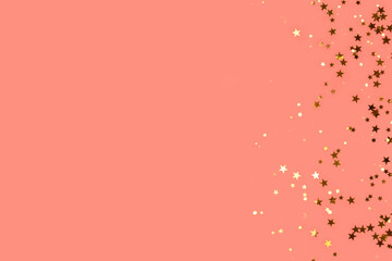 Trendy gold colored stars confetti scattered on a coral background with place for text.
