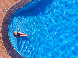 Fototapeta na wymiar Aerial drone top view, carefree female tourist in black swimsuit relaxing while lying near pool enjoying summer vacation holidays.Young woman resting