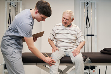 Manual therapist touching aching knee of elderly person