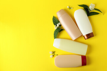 Blank bottles of shampoo and flowers on yellow background