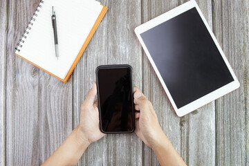 Closeup mockup image of man using digital mobile phone and tablet with blank screen on wooden table.