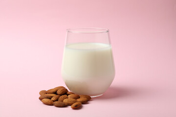 Glass of milk and almonds on pink background