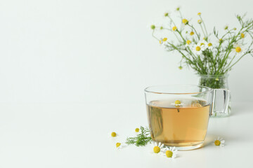 Cup of chamomile tea and ingredients on white table