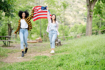 Carefree multiethnic couple of women running with American flag