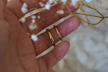 A touching, gentle photo of a woman's hand with gold wedding rings on an unnamed finger against the...