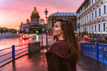 Obraz na płótnie Canvas A young woman walks during a pink sunset in the center of St. Petersburg with a view of St. Isaac's Cathedr