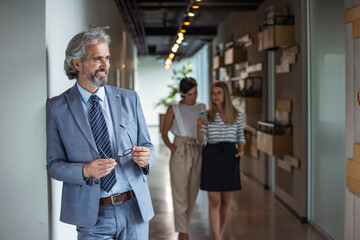 Portrait of young happy businessman wearing grey suit and white shirt standing and smiling. Multiethnic satisfied man with beard and eyeglasses feeling confident at office.