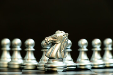 Silver knight piece stand in fron of silver pawn team on black background (Concept for leader,...
