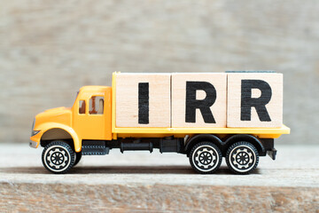 Toy truck hold alphabet letter block in word IRR (Abbreviation of internal rate of return) on wood background