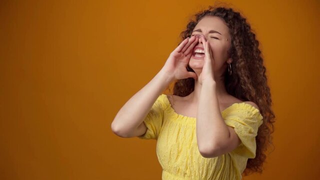 Young curly haired woman shouting against yellow background