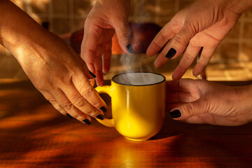 Quatro mãos, femininas, com unhas pintadas de preto, pegando uma caneca amarela com uma bebida...