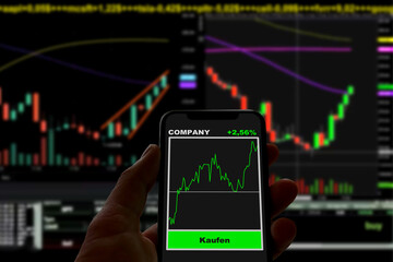 Person hält Smartphone mit einer Neo-Broker App vor einem Bildschirm mit verschiedenen Aktiencharts, Aktienhandel, Börse, Digitalisierung, Finanzen, Geldanlage, Investieren