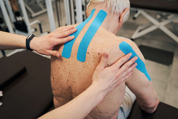 Orthopedist fixating kinesiology therapeutic tape on man back