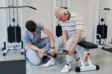 Physiotherapist helping old man in fixating his ankle straps