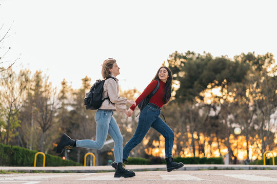 two student girls crossing crosswalk holding her hands, running and smiling