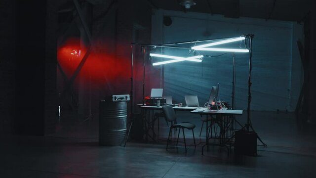 Slowmo tracking wide shot of dark industrial space with desks and computers Hackers hideout with red and blue lighting
