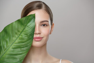 Portrait of woman and green leaf. Organic beauty. Gray background. - obrazy, fototapety, plakaty
