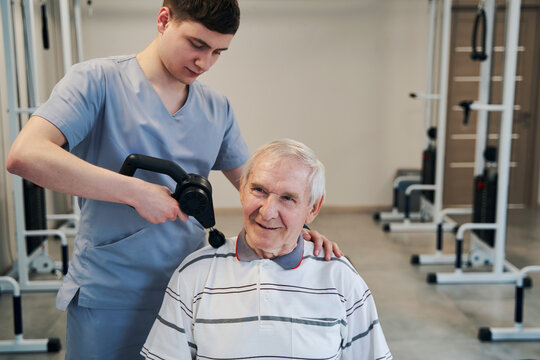 Orthopedist Using Percussion Massager On Aged Male Shoulder