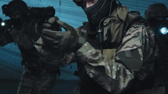 Slowmo tilt up shot of armed SWAT team in uniforms raiding terrorist hideout Officer with gun talking on walkie-talkie